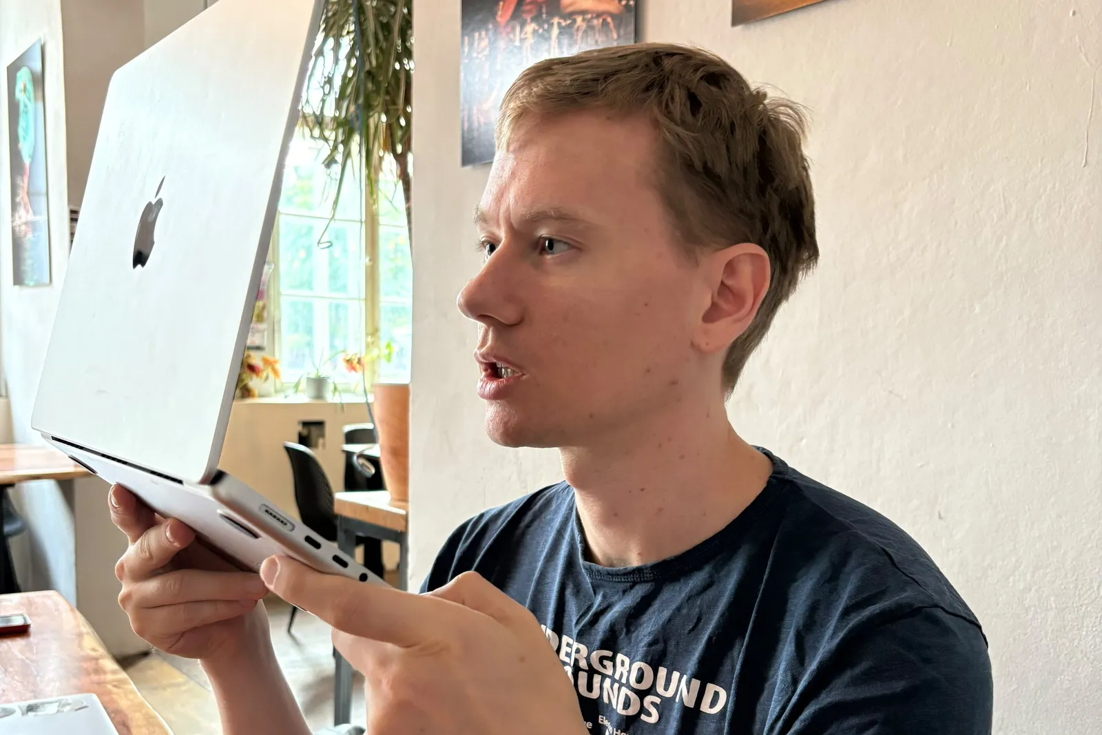 Olof holding an open laptop close to his face while dictating in a café.