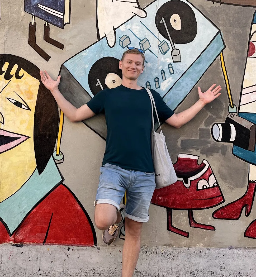 Olof smiling with his arms outstretched in front of a colorful mural.
